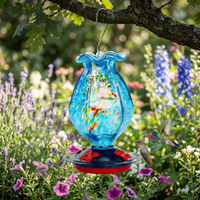 Glass bird feeder hanging from a tree branch in a garden